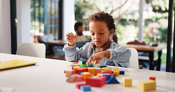 istock Learning, kid or playing with building blocks in home for fine motor skills, problem solving or creativity. Education, african boy and toys on table for cognitive development and sensory imagination 2248323805
