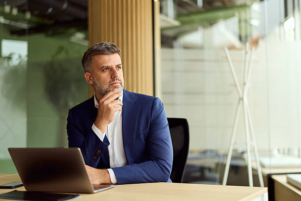 Thoughtful Professional In Blue Suit At Desk With Laptop In Modern Office