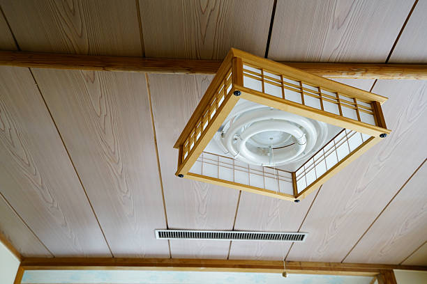 A Japanese-style ceiling light with a wooden lattice frame and circular lamp, mounted on a simple wood-paneled ceiling with clean, minimalist interior details.