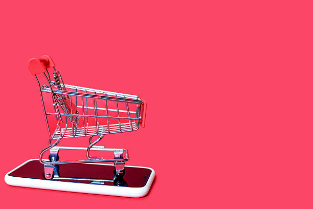 A toy basket stands on a mobile phone on a red background. The concept of online shopping using the phone. Convenience of shopping with the help of modern technologies in the form of a mobile phone