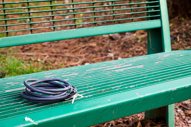 An electrical cable coiled on a green, public bench