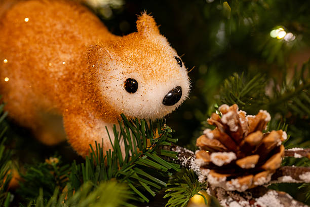 Close-up of a glittery squirrel ornament nestled among green pine needles beside a frosted pinecone. Warm golden lights create a cozy holiday ambiance with soft bokeh and rich textures. Perfect for Christmas marketing, product displays, packaging, social posts, and seasonal design.
