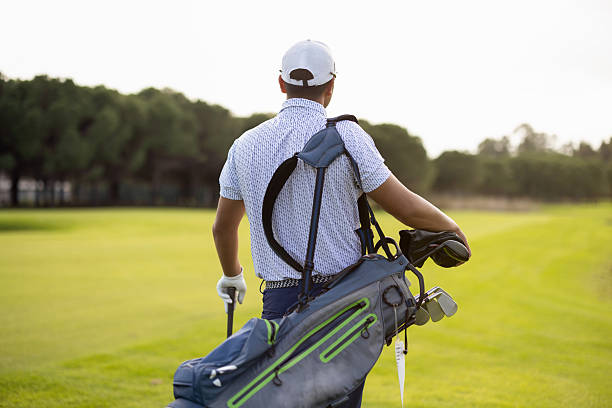 A golfer carrying a full club bag while walking across a bright, sunlit fairway. The image reflects the calm, focused atmosphere of outdoor sports, making it ideal for themes of golf training, leisure, recreation, and athletic lifestyle.
