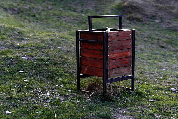 Wooden trash bin with metal frame placed on grassy terrain outdoors, ideal for themes of cleanliness, environment, and public spaces.