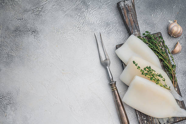 istock Raw calamari arranged with herbs on weathered wood against a gray stone backdrop ideal for culinary seafood stock concepts. 2248354926