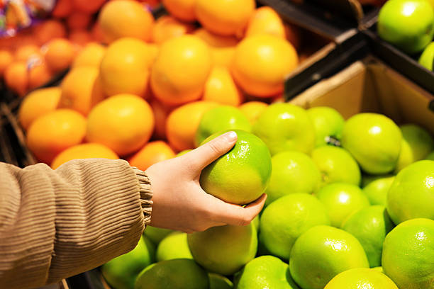 istock A customer's hand selects a large, bright green citrus fruit a pomelo from a pile, with blurred orange fruit in the background. 2248357138
