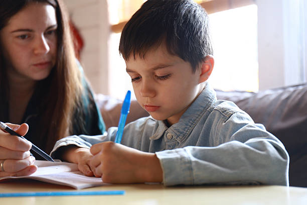 istock mom is doing her homework with her child. The boy is learning to write letters 2248358331