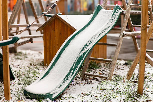 Snow covered green children's slide in a backyard playground, with wooden play structures around it.