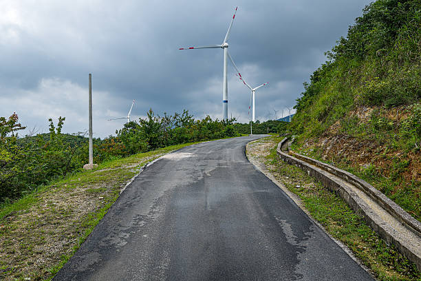 Vacant highway curving through a mountain range with wind farms visible in the distance.