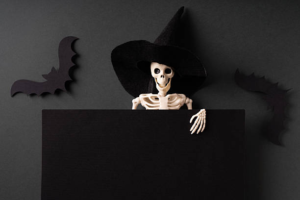 istock Skeleton in witch hat with blank black board on dark background 2248359525