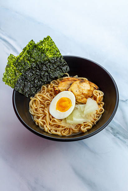 istock Ramen with egg noodles, char siu chicken, and fresh pickles, in a savory broth on a light background 2248361850