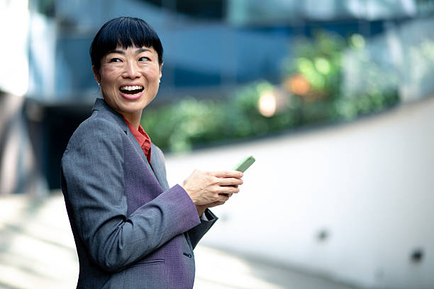 istock Asian businesswoman laughing while using smartphone outdoors. Stock image 2248361882