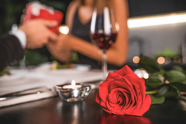 istock Young man giving his girlfriend gift box for present. focus on rose and candle on foreground. Anniversary gift, surprise for Valentine`s day. Relationship and dating 2248362433