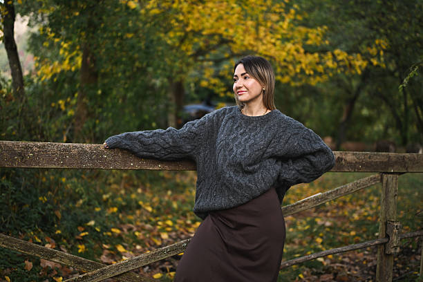 Woman standing by wooden fence wearing cable knit sweater in autumn park