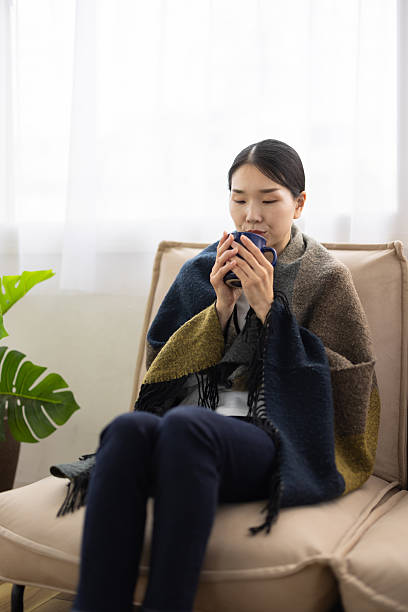 Woman Wrapped in Blanket Blowing on Hot Drink in Mug
