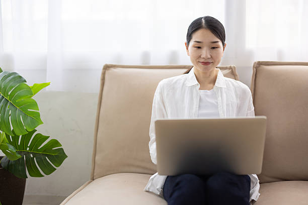 istock Woman Sitting on Sofa Using Laptop in Bright Living Room 2248365402