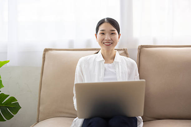 istock Woman Sitting on Sofa Using Laptop in Bright Living Room 2248365456