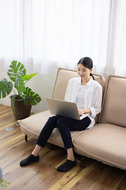 Woman Sitting on Sofa Using Laptop in Bright Living Room