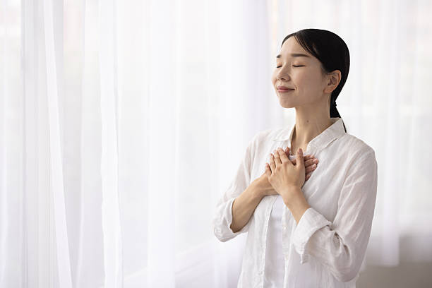 istock Woman Standing by Window with Hands on Chest in Peaceful Reflection 2248365740