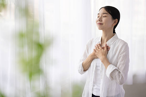 Woman Standing by Window with Hands on Chest in Peaceful Reflection
