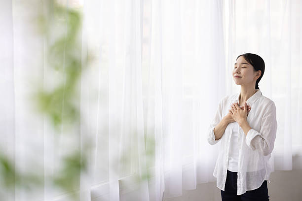 istock Woman Standing by Window with Hands on Chest in Peaceful Reflection 2248365814