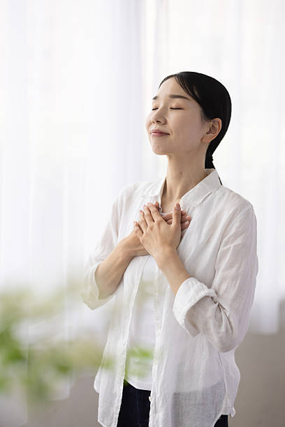 istock Woman Standing by Window with Hands on Chest in Peaceful Reflection 2248365826