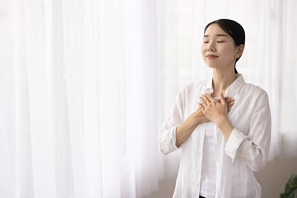 istock Woman Standing by Window with Hands on Chest in Peaceful Reflection 2248365846