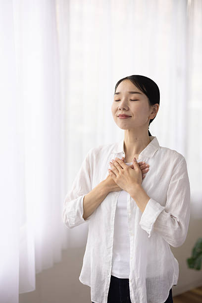 istock Woman Standing by Window with Hands on Chest in Peaceful Reflection 2248365854