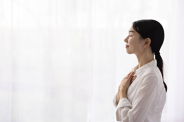 istock Woman Standing by Window with Hands on Chest in Peaceful Reflection 2248365865
