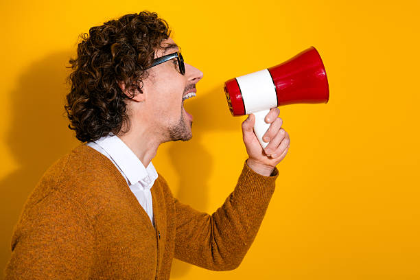 istock Young man with megaphone shouts against a bright yellow background for bold advertisement and stylish lifestyle 2248366390