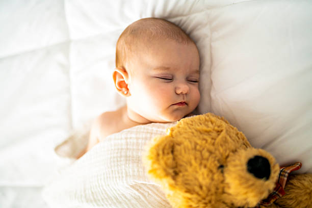 istock A 4 month baby sleeping on a white bed at home with bear 2248367089