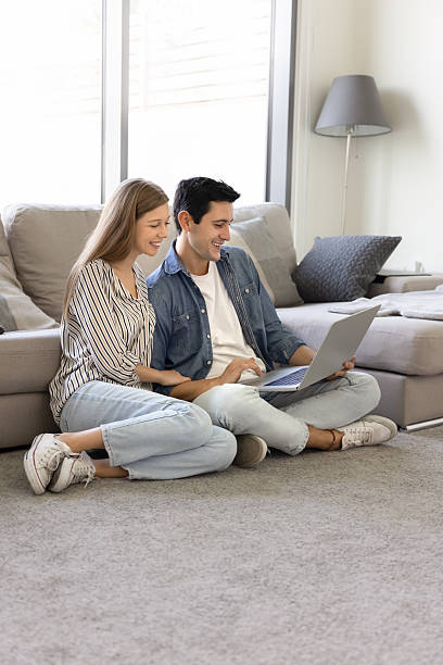 istock Young couple using laptop sit comfortably on carpeted floor 2248367964