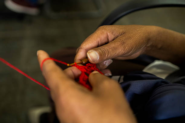 Close-up of hands knitting with red yarn using a crochet hook. The image highlights craftsmanship, manual work, and traditional handmade techniques.