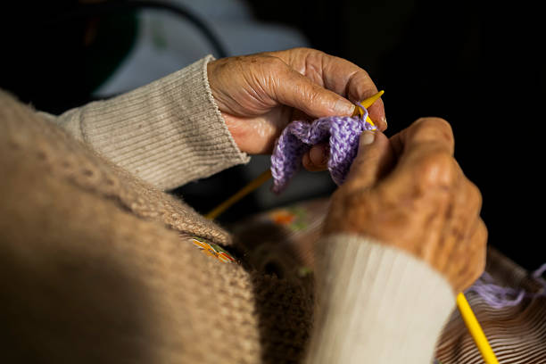 Close-up of hands knitting with red yarn using a crochet hook. The image highlights craftsmanship, manual work, and traditional handmade techniques.