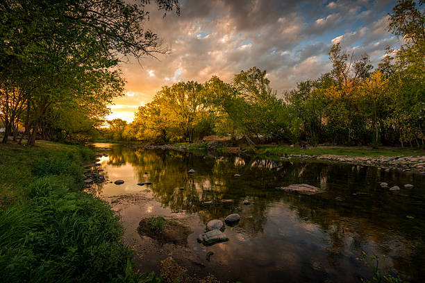 istock River reflecting golden sunset sky and green trees 2248372547
