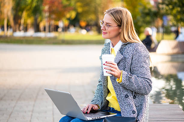 istock Female remote worker drinking coffee and using laptop in the public park 2248373384