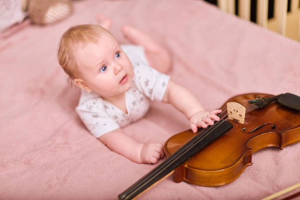 istock Curious baby girl with violin on soft pink bedding 2248375427