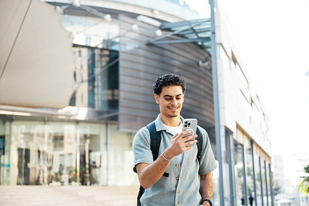 istock Handsome young man in the high street with backpack commuting to work. Entrepreneur is using smart phone while on the go 2248375624