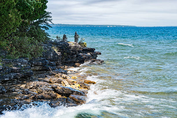 The calm waters of Lake Michigan gently crash against the rocky shoreline at Cave Point. Cairns are stacked on the rocks, showcasing human creativity in nature.