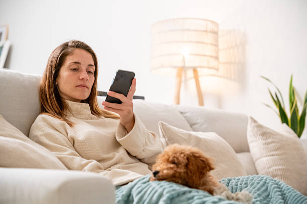 istock Woman relaxing on couch using phone with dog 2248381554