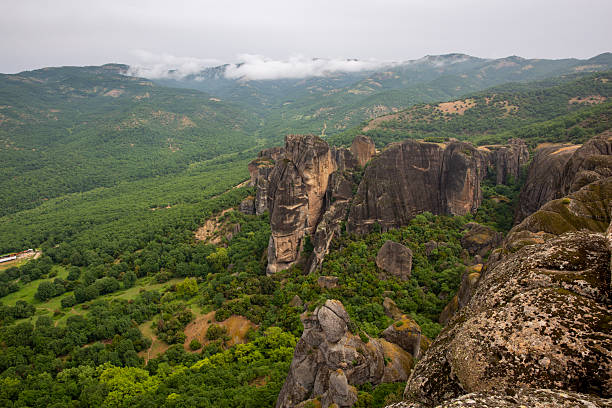 Unesco world heritage site meteora rock formations towering over a lush green valley with distant mountains and cloudy skies in greece, unesco world heritage site. Meteora, greece