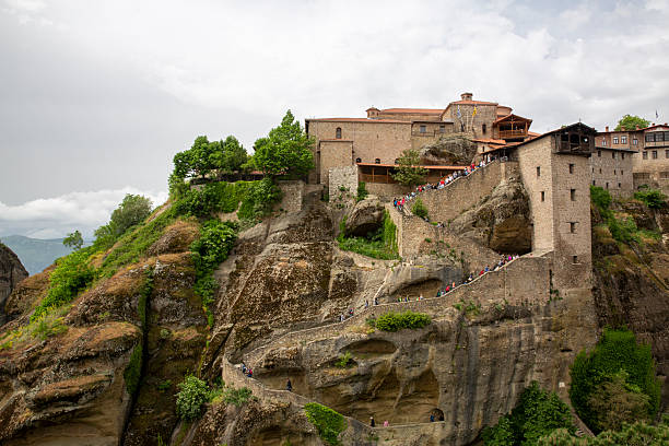 Meteora monastery in greece with many tourists climbing stone steps to the ancient cliff top complex