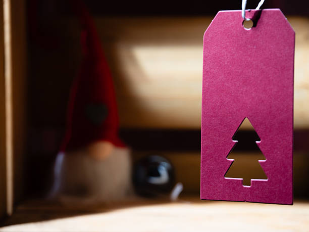 Red gift tag and Christmas gnome with bauble on wooden box background