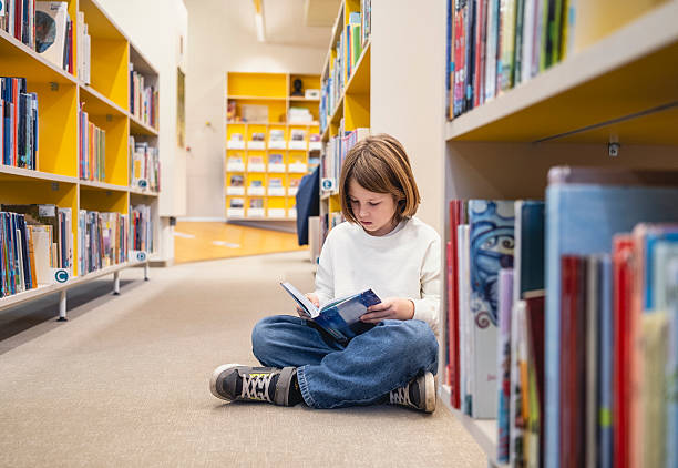istock Focused Caucasian Child Reading Book on Library Floor 2248386064