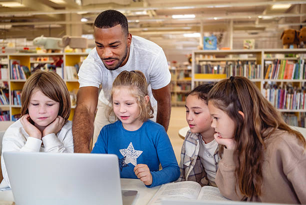 istock Diverse Children Engaged with Technology in Library Setting Guided by Teacher 2248386156