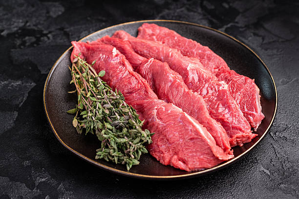 Raw sliced horse meat steaks presented with herbs and spices, inviting creativity in the kitchen for those seeking bold flavors and unique dining experiences. black background. top view
