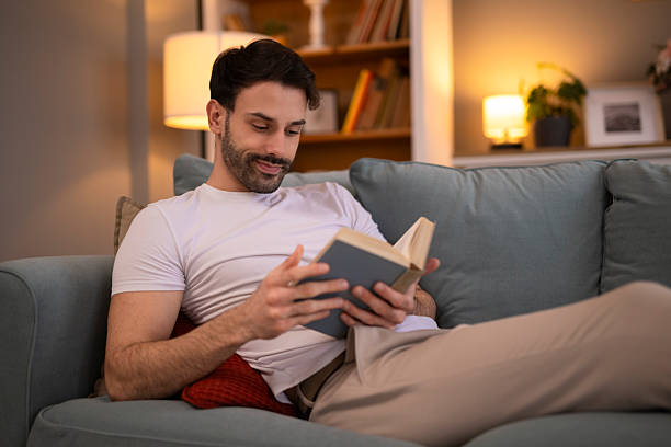 istock Young man relaxing on sofa reading book at home 2248394750