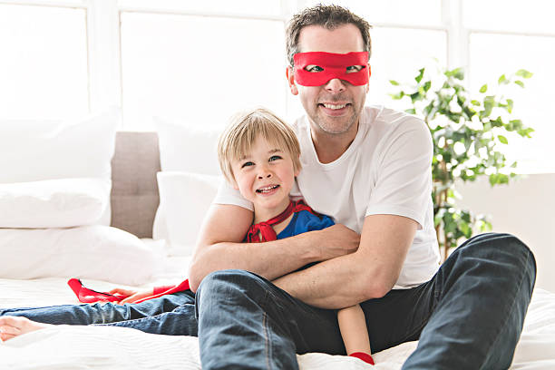 A Father and son play superheroes on bed at home