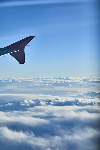 A tranquil travel scene captured from inside an airplane, showing the wing against a clear blue sky and soft clouds below. Ideal for themes of flight, journey, adventure, and exploration.