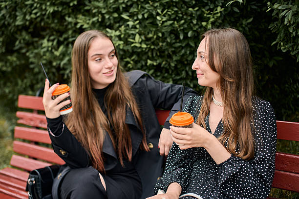 istock Young girlfriends gossiping with coffee on park bench in daylight 2248401377